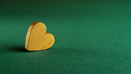 Golden valentine heart against textured bottle green background macro with copy space. Wide blank mockup for Valentine day holiday, greeting card and banner. Symbol of love and passion.の写真素材