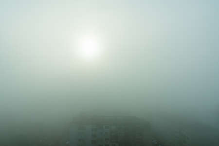 The morning sun barely breaks through the dense fog. Heavy fog obscuring streets and buildings. City...