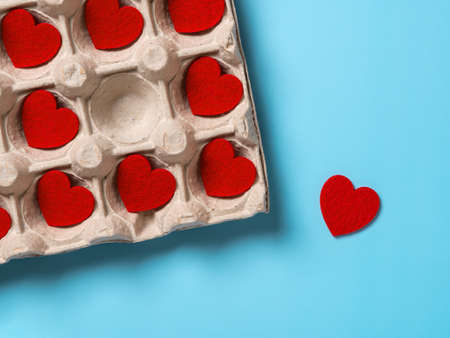 One Valentine heart taken out from the full cardboard tray against turquoise background. To break someone heart, heartbreaker and irresponsibility in emotional relationships concepts. Top view.の写真素材