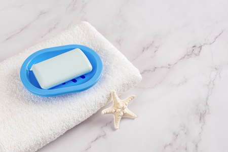 Rectangular soap bar on a blue dish on a white cotton terry towel and five finger knobby starfish...