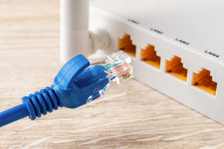 Blue network cable plug almost inserted into the yellow socket of white wi-fi wireless router. Wlan...
