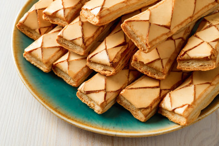 Heap of Italian crispy bakery Sfogliatine glassate biscuits on a turquoise plate over wooden table....