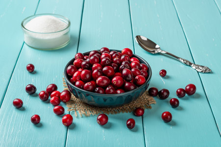 Fresh red cranberries in a blue ceramic bowl, spoon and sugar on a turquoise wooden table. Ingredient for Thanksgiving and Christmas dishes and desserts. Wild berries for healthy eating. Close-up.の写真素材