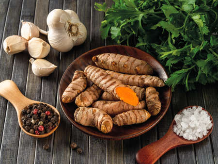 Raw organic turmeric curcuma roots, garlic cloves, pepper grains, sea salt and fresh parsley on a...