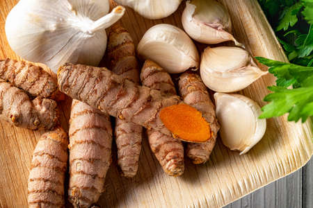 Raw organic curcuma roots and garlic cloves on a wooden plate close-up. Fresh whole turmeric...