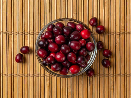 Fresh ripe cranberries in a glass bowl over brown bamboo table mat. Red wild berries for...