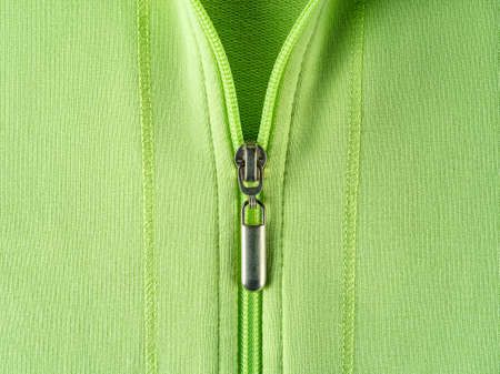 Zip fastener of light green sweatshirt hoodie close-up. Fashionable summer cotton jacket with zipper fastening. Trendy clothes in bright colors, casual outerwear concepts. Half zipped pullover. Cropped image.の写真素材