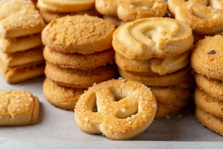 Sugar pretzel against of stacked shortbread cookies on a white baking parchment. Assorted crispy...