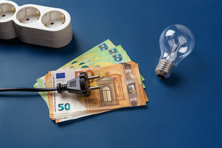 Black power plug on 50 euro banknotes and light bulb over blue background. High energy costs due to power crisis and inflation concepts. Increasing the costs of electricity, heating and cooling. Top view.の写真素材
