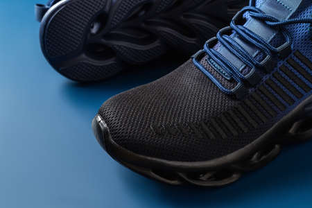 Grooved sole men sneakers of black blue colors on a blue background. Pair of new mesh textile shoes for active lifestyle and fitness. Modern sport shoes with laced fastening concept. Close-up.の写真素材