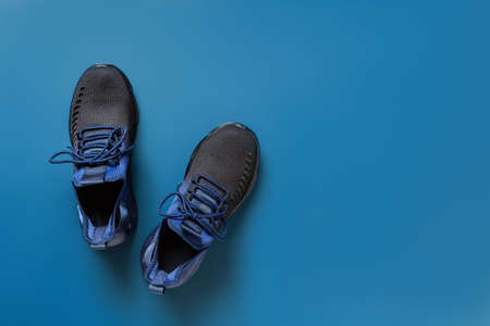 Pair of new textile sneakers over blue background. Black blue sport shoes with laced fastening...