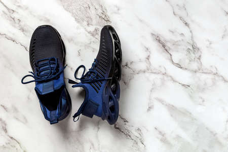 Laced up grooved men shoes on a marble floor. Pair of black blue mesh fabric sneakers for fitness and active lifestyle. New textile sneakers with laced fastening. Sport shoes concept. Top view.の写真素材