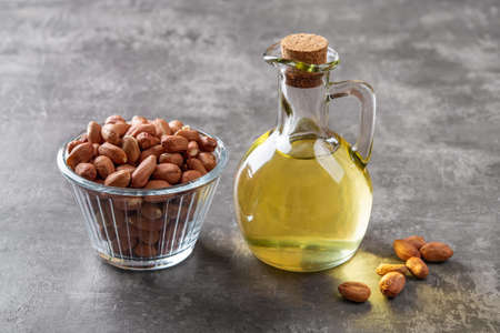Peanut oil in a glass jug and raw peeled groundnut in a glass bowl over gray background. Arachis hypogaea as edible seeds and oil crop. Monounsaturated cooking oil. Vegetarian snack. Top view.の写真素材