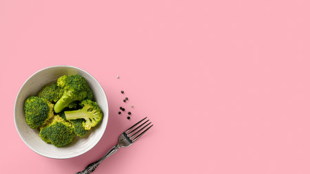 Raw green broccoli florets in a bowl and fork against soft pink colored background. Concept of low calorie antioxidant detox dieting. Vegetarian vitamin food. Wide banner. Copy space. Top view.の写真素材