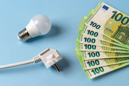 Electricity price spike. White electrical plug, light bulb and 100 euro banknotes in a fan shape...