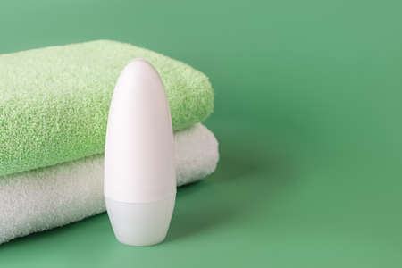 Roll on antiperspirant deodorant and bath towels on a green background. Cosmetics to reduce perspiration. Concept of personal hygiene items, body care, toiletries. Copy space. Front view.の写真素材