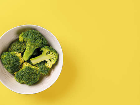Raw green broccoli florets in a bowl against yellow background. Vitamin vegetarian food recipe. Concept of cooking low calorie vegetables for antioxidant dieting. Copy space. Top view.の写真素材