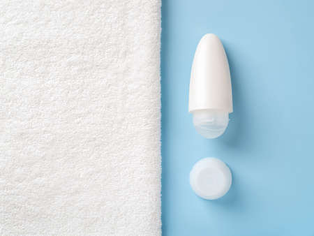Roll on antiperspirant deodorant over blue background next to white bath towel with copy space. Purity, body care, toiletries and personal hygiene items concept. Cosmetic product mockup. Closeup.の写真素材