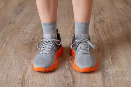 Gray sneakers and gray socks on the woman feet. Standing feet shod in mesh sneakers with grooved orange sole on the floor. New shoes for active lifestyle, everyday life and sports. Low angle view.の写真素材