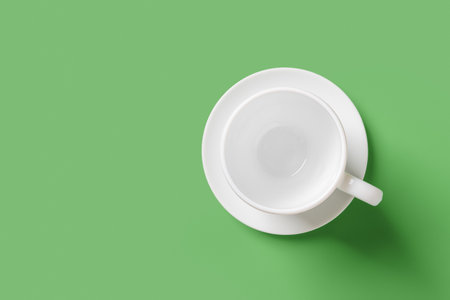 White mug over green background. Empty cup on a saucer closeup. Large teacup mockup for hot beverages design. Porcelain tableware and modern crockery concept. Copy space. Top view.の写真素材