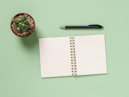 Blank notebook, pen and cactus over green background. Paper notepad for writing life goals, day organizing and business planning. Making to do list mock up. Copy space. Top view.の写真素材