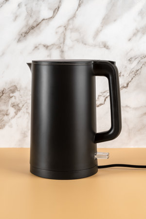 Matte black kettle against marble wall. Stylish electric kettle for heating water to boiling for tea and coffee. Class 1 electrical appliances for kitchen. Vertical frame. Front view.の写真素材