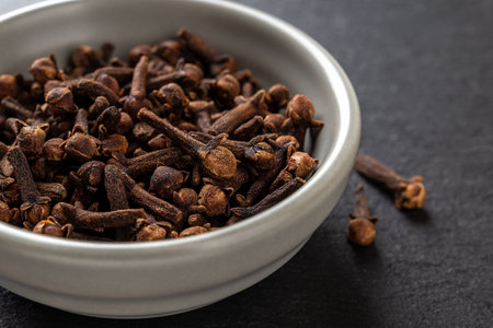 Whole cloves spice in a bowl over black background. Dry clove buds in a gray ceramic bowl macro. Cooking, herbal medicine and spice concept. Close-up.の写真素材