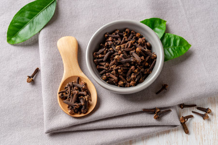 Whole cloves spice over gray textile background. Dry organic clove buds in a small bowl and wooden spoon macro. Spice, condiment and cooking concept. Top view.の写真素材