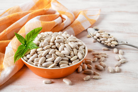 Raw kidney beans in a bowl over white wooden background. Orange bowl full of dry organic white...