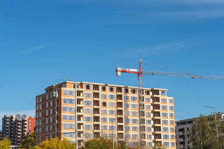 Ð¡onstruction of a multi-storey residential building on a sunny day. Brick house under construction and tower crane against blue sky. Ð¡onstruction industry concept. Front view.の写真素材