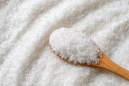Monosodium glutamate in a wooden spoon over E621 white crystals background. Full spoon of MSG macro. Common food additive, flavor enhancer concept. Top view.の写真素材