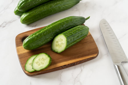 Cut in half cucumber on a wooden cutting board. Cooking vegetarian salad of green long cucumbers. Organic vegetables, healthy eating, harvest concept. Top view.の写真素材