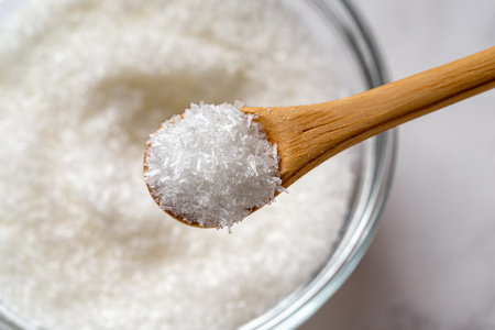 Wooden spoon full of monosodium glutamate over MSG white crystals in a glass bowl macro close-up. Concept of flavor enhancer food additive E621. Top view.の写真素材