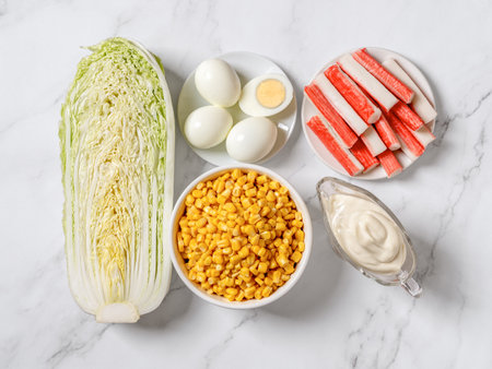 Ingredients for cooking homemade salad: canned corn, surimi sticks, half of napa cabbage, boiled eggs and mayo on a marble countertop. Mom's salad recipe. Top view.の写真素材
