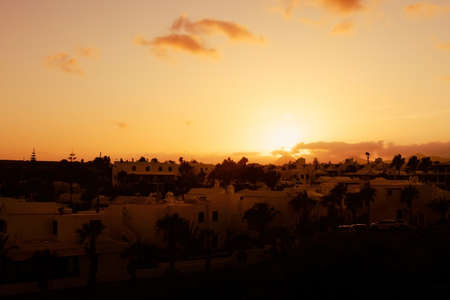 An orange sun sits low on the horizon, illuminating the sky and sillhouetting the clouds and...