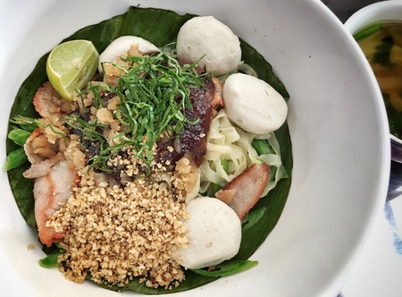 A bowl of spicy thai style egg noodle with red pork crunch peanut and pork ballの素材