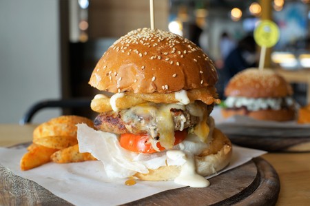 Huge beef burger with fried onion and tomato on wooden plateの写真素材