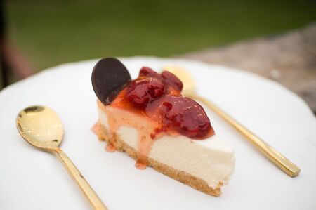 Homemade strawberry cheesecake topping with strawberry jam on white plate with golden spoonの写真素材