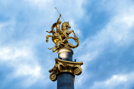 Golden statue of St. George slaying the dragon, standing proudly atop a towering column in Tbilisi,...