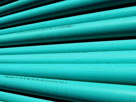 PVC plastic pipe stacked at the construction site ready to be laid as a sewer line; bright highlights and deep shadows make interesting abstract pattern.  Good background for your text.の写真素材