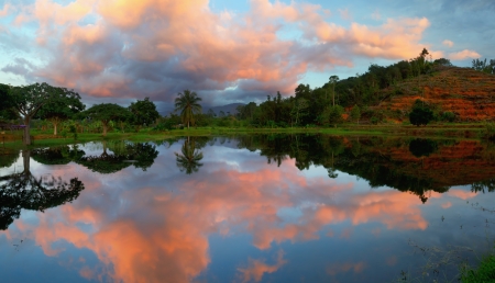 Reflection of sunset colored clouds with trees and hills at a lake in Borneo, Sabah, Malaysiaの写真素材