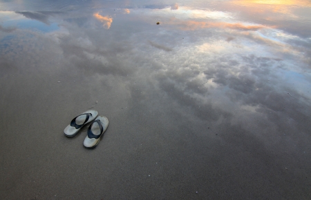 Slippers on a sandy beach with reflection of sunsetの写真素材