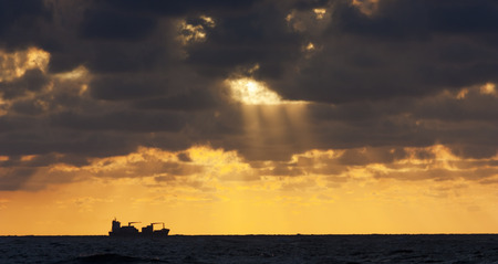 Silhouette of a ship at sunset with sunraysの写真素材