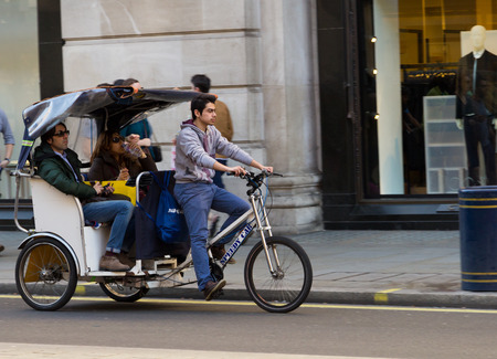LONDON, UK - 16TH MARCH 2014  A man riding a Rickshaw with some passengers in the back down a street in Londonのeditorial素材