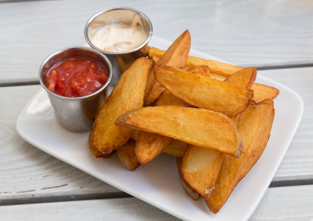 Plate of fries and sauces on a table outside.