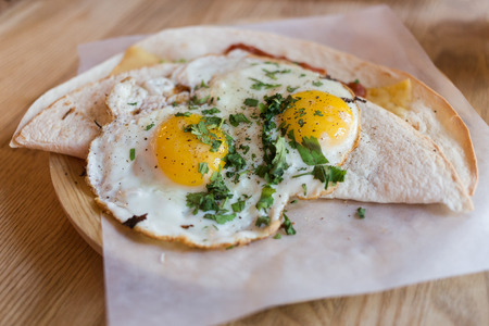 Fried eggs on a folded  tortilla  wrap with fresh seasoning. Served on a wooden plate and baking paper.の写真素材