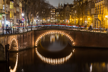 A view of the bridges at the Leidsegracht and Keizersgracht canals intersection in Amsterdam at dusk. Bikes and buildings can be seen. The trail of traffic can be seen on a bridge.の写真素材