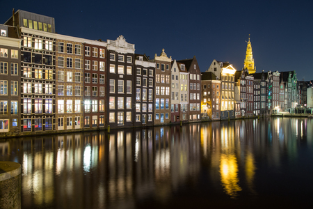 Old Buildings along the Damrak in Amsterdam at night. Reflections can be seen in the water.の写真素材