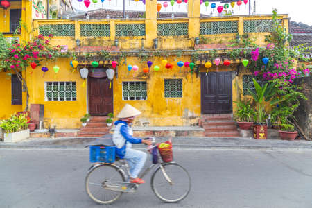HOI AN, VIETNAM - 25TH MARCH 2017:  Streets in Hoi An Ancient Town during the morning. Showing colourful architecture and a person going past on a bike and conical hat.のeditorial素材