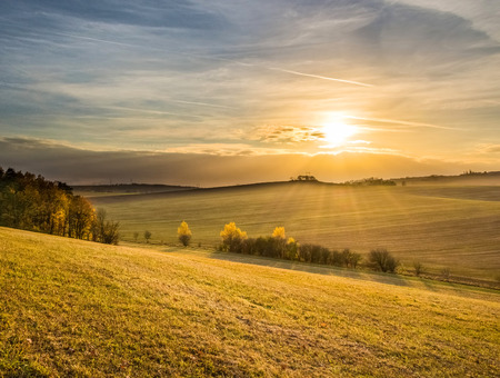 Amazing sunset in colorful autumnal landscape with sun, pastures and treesの写真素材